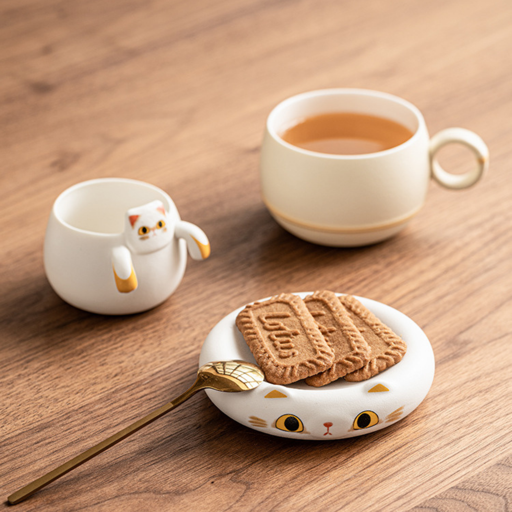 Ceramic cat-shaped cup, saucer with cookies, and spoon on a wooden surface