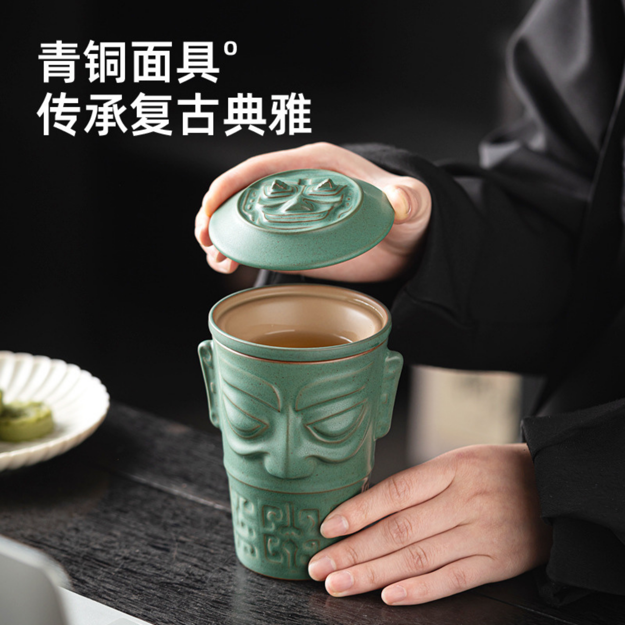Person holding a green ceramic mug with face design on a dark surface