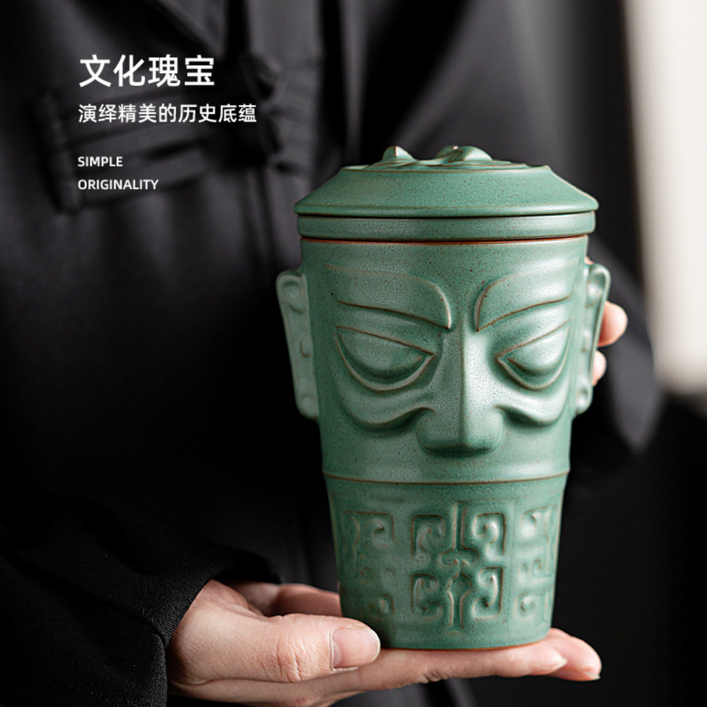Ceramic mug with face design held by a person, against a blurred background