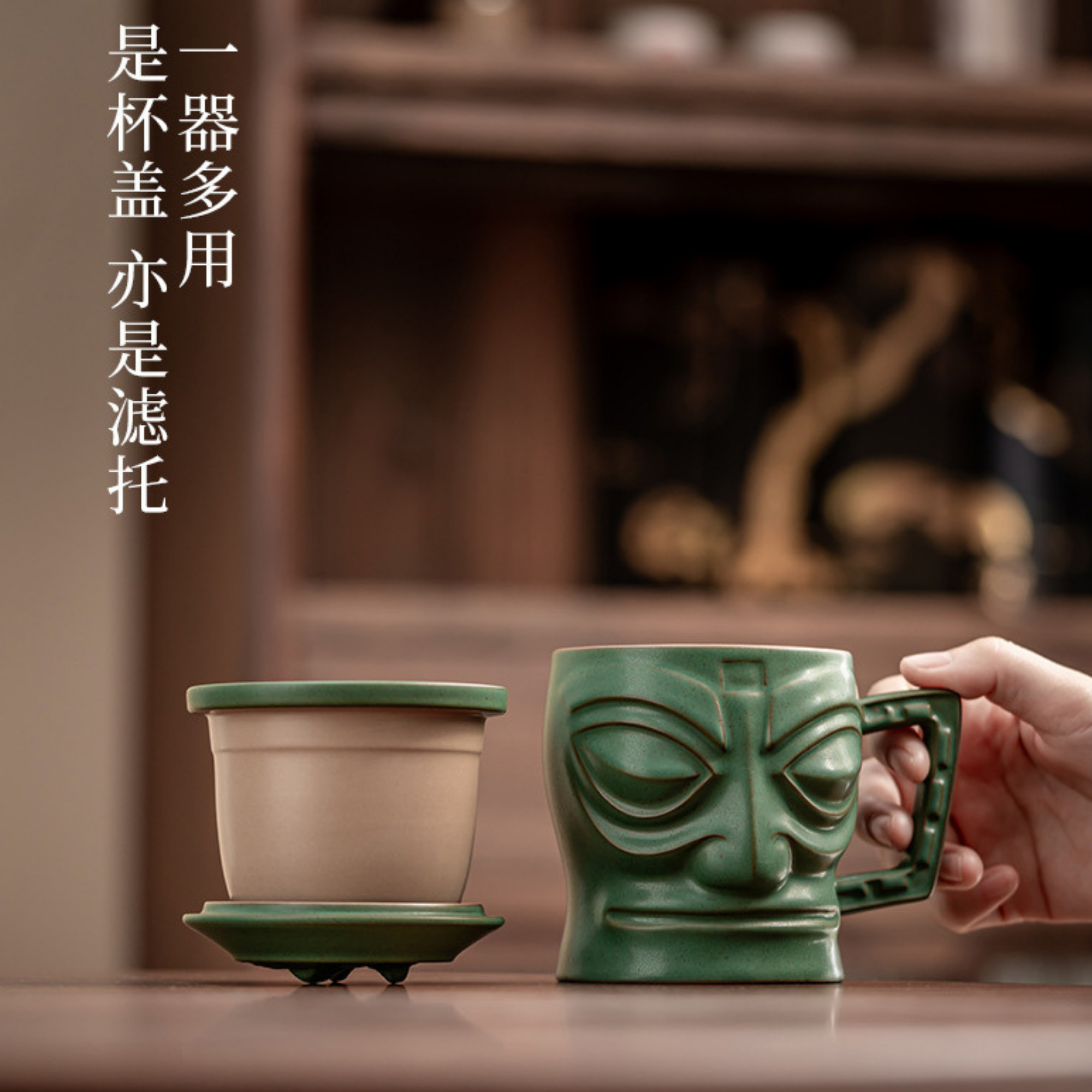 Green ceramic mug with face design held by a hand, next to a matching pot on a wooden surface.